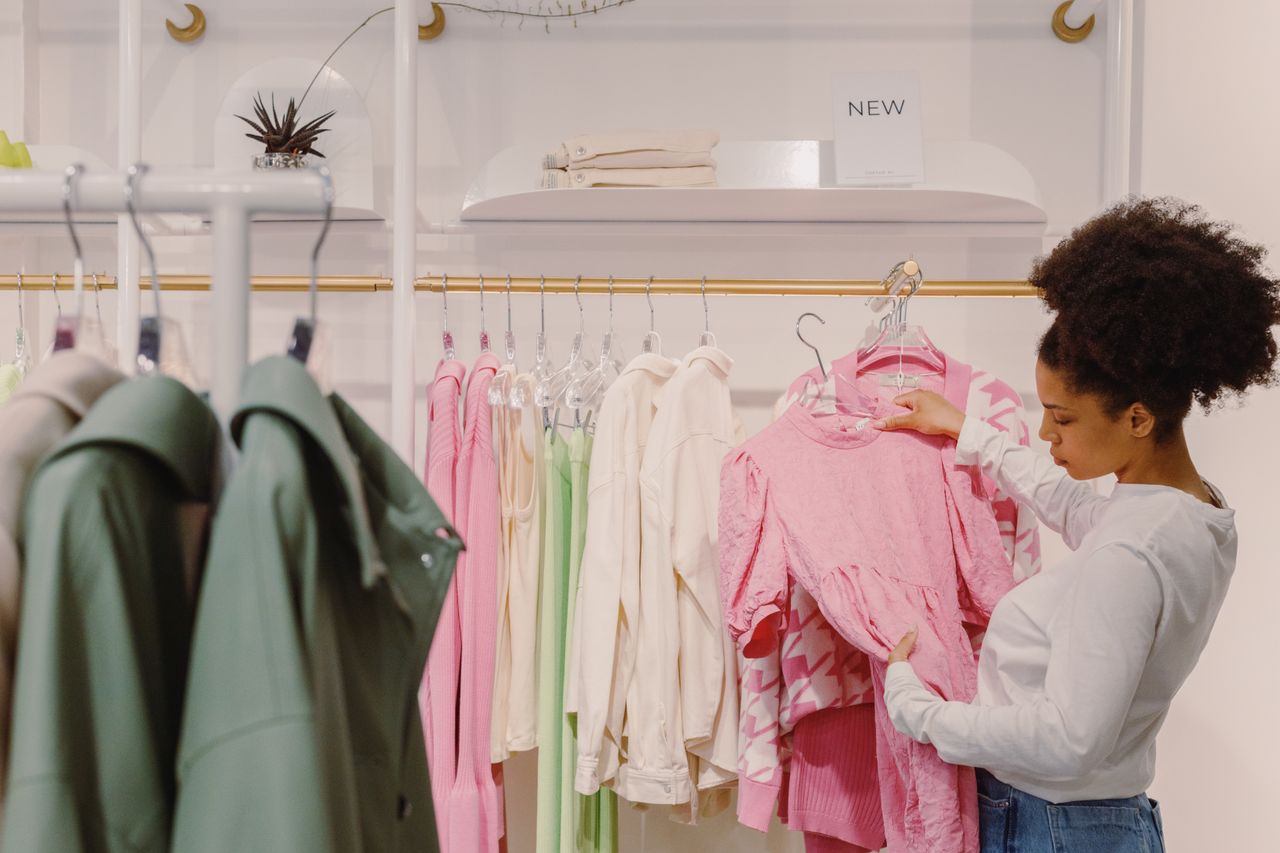 embark A stylish woman explores pink and pastel outfits in a modern boutique.