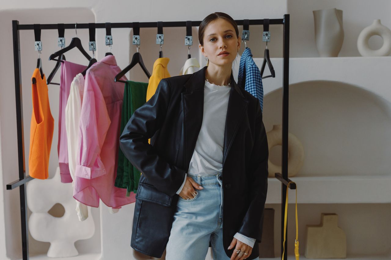 gallery-06 Stylish woman in a black leather jacket poses beside a clothing rack in a chic boutique.